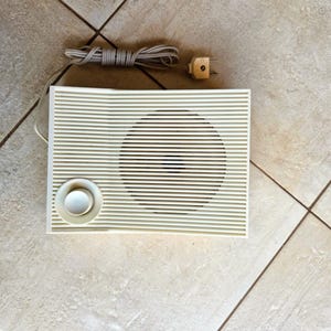 May include: A white vintage radio with a single speaker and a round knob. The radio has a cord with a plug.