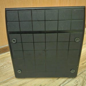 Może przedstawiać: Czarna kwadratowa platforma z wzorem siatki i czterema małymi okrągłymi czarnymi akcentami na dole.