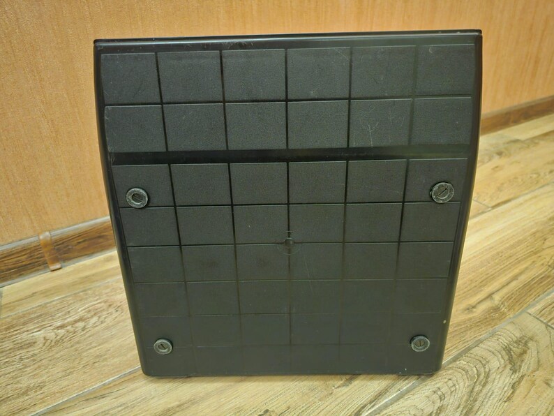 Może przedstawiać: Czarna kwadratowa platforma z wzorem siatki i czterema małymi okrągłymi czarnymi akcentami na dole.