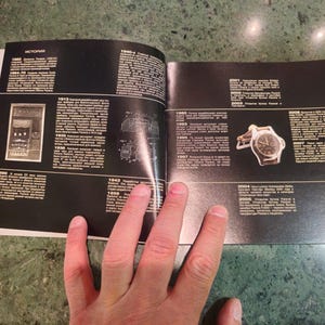 Pu&ograve; includere: Un libro bianco e nero aperto a una pagina con una cronologia di orologi Rolex. La pagina presenta un'illustrazione in bianco e nero di un orologio e una foto di un orologio Rolex argentato con quadrante nero.