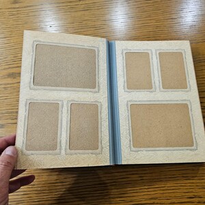 May include: A white photo album with a blue spine and five empty photo slots. The album has a decorative border around each photo slot.