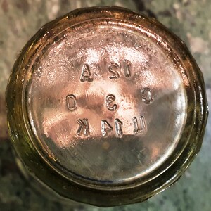 May include: Close-up of the bottom of a clear glass bottle with the text "T.I.A.K. 3 C.I.S.A" embossed on the bottom.