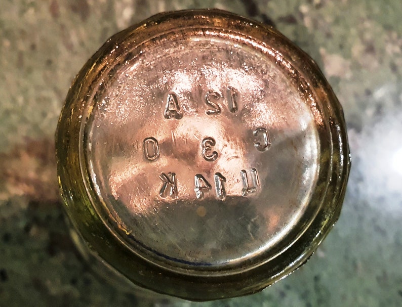 May include: Close-up of the bottom of a clear glass bottle with the text "T.I.A.K. 3 C.I.S.A" embossed on the bottom.