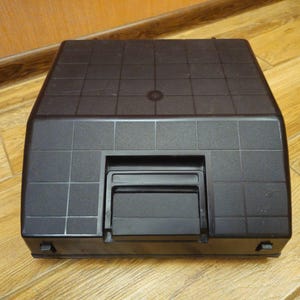 Może przedstawiać: Czarna maszyna do pisania z fakturowanym wierzchem i czarną plastikową osłoną nad klawiszami.