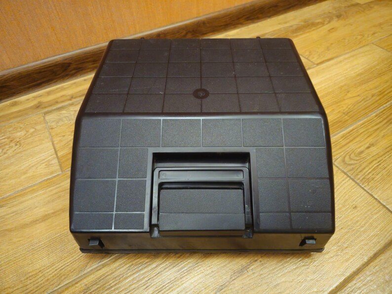 Może przedstawiać: Czarna maszyna do pisania z fakturowanym wierzchem i czarną plastikową osłoną nad klawiszami.