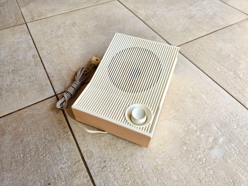 May include: A vintage white speaker with a round knob and a cord. The speaker has a wood trim around the edges.