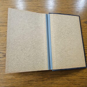 May include: An open book with a blue cover and patterned endpapers. The book is lying open on a wooden surface.