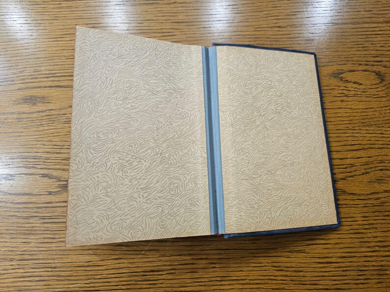 May include: An open book with a blue cover and patterned endpapers. The book is lying open on a wooden surface.