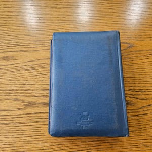 May include: A blue hardcover book with a small emblem on the front. The emblem is a white ship with a red flag and the text "2000" underneath.