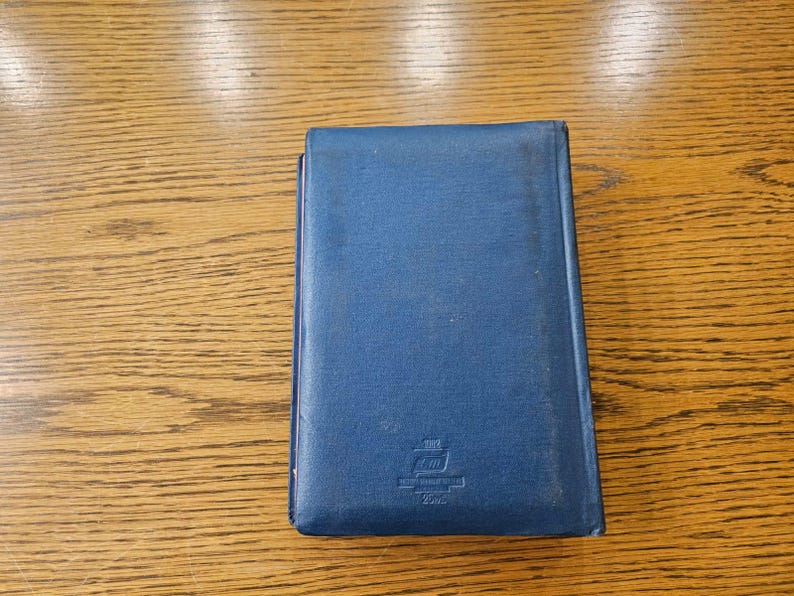 May include: A blue hardcover book with a small emblem on the front. The emblem is a white ship with a red flag and the text "2000" underneath.