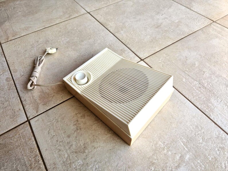 May include: A vintage, off-white, rectangular speaker with a round knob and a speaker grille. The speaker is sitting on a light brown tiled floor.