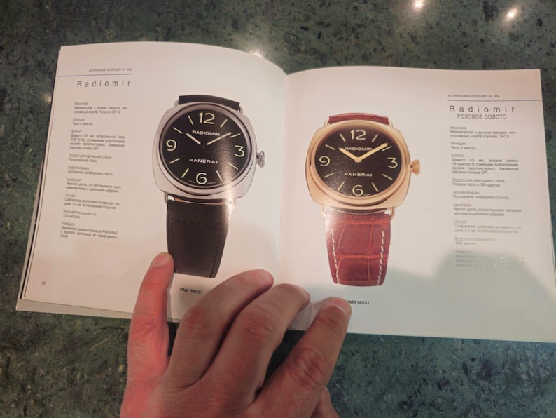 Pu&ograve; includere: Due orologi da polso con quadranti neri e indici orari in numeri romani. L'orologio a sinistra ha un cinturino in pelle nera e l'orologio a destra ha un cinturino in pelle marrone. Il testo "Radiomir" e "Radiomir ROSOVO ZOROTO" &egrave; visibile sulla pagina.