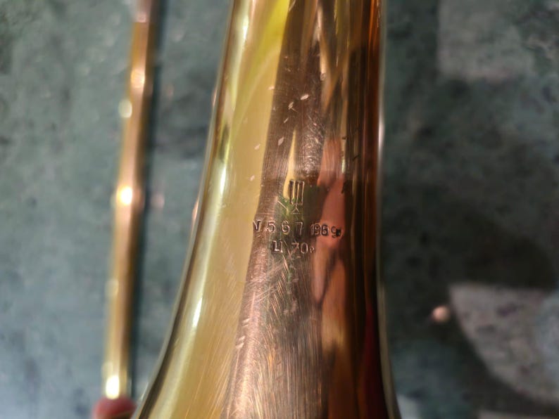 May include: Close-up of a gold trombone bell with the inscription "V 567 188* L 700" engraved on the side.