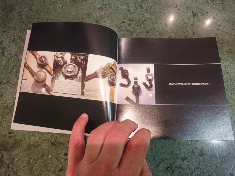 Pu&ograve; includere: Un libro aperto con una copertina nera. La pagina sinistra mostra un primo piano di diversi orologi vintage con cinturini in pelle. La pagina destra mostra un primo piano di diversi orologi neri con cinturini in metallo. Il testo "историческая коллекция" &egrave; stampato sulla pagina destra.