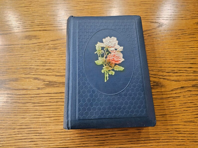 May include: A blue hardcover book with a floral design on the front cover. The design features a bouquet of pink and white roses with green leaves.