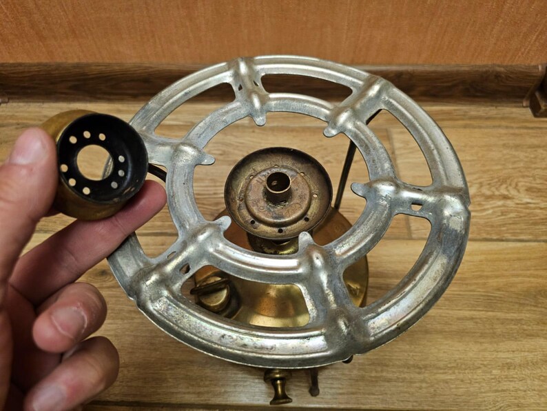 K&ouml;nnte beinhalten: Ein antiker Herdbrenner aus Messing mit einem runden Metallrost und einer zentralen Brenner&ouml;ffnung. Der Brenner hat ein dekoratives Design mit einer Reihe konzentrischer Kreise und einem erh&ouml;hten Rand.