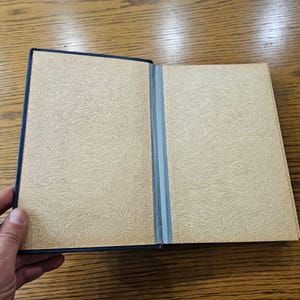 May include: A closed book with a blue cover and a cream-colored interior. The book has a textured pattern on the cover.