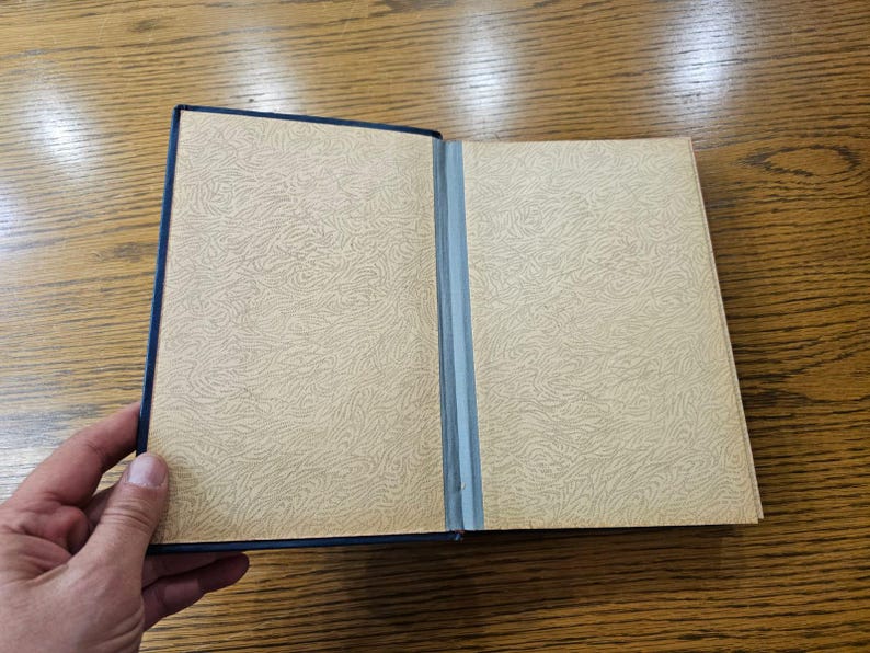 May include: A closed book with a blue cover and a cream-colored interior. The book has a textured pattern on the cover.