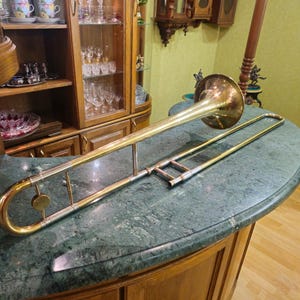 May include: A gold-colored trombone with a silver slide. The trombone is lying on a green marble surface.