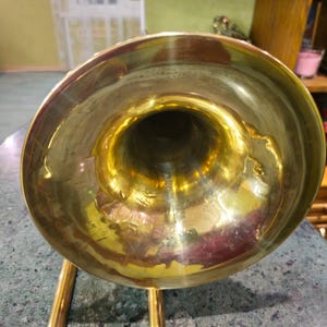 May include: A gold-colored trombone bell with a shiny finish. The bell is the wide, flared end of the trombone.