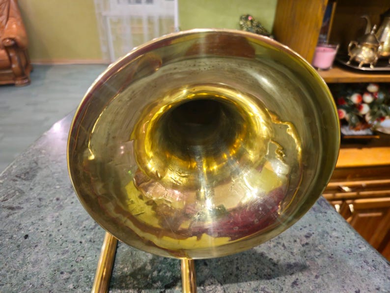 May include: A gold-colored trombone bell with a shiny finish. The bell is the wide, flared end of the trombone.