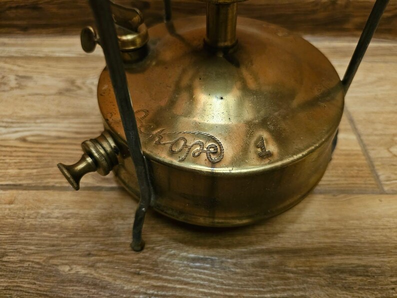K&ouml;nnte beinhalten: Campingkocher aus Messing mit einem schwarzen Metallst&auml;nder und einem Etikett mit der Aufschrift "Primus 1".