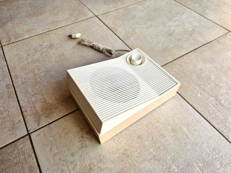 May include: A vintage white and beige speaker with a round knob on the top. The speaker has a grill covering the speaker cone.