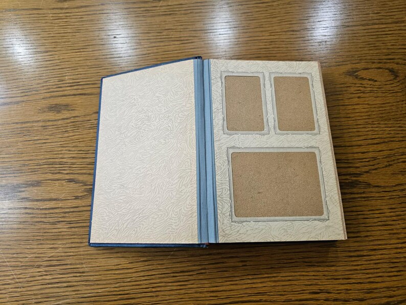 May include: A blue photo album with a white patterned cover and three rectangular photo slots on the inside cover.