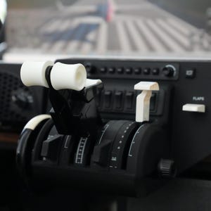 May include: A black flight simulator control panel with white knobs and switches. The panel has a flap lever, a throttle lever, and a variety of other controls. The panel is made of plastic and metal.