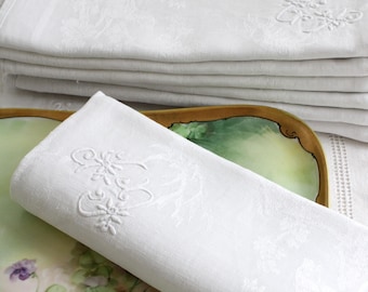 May include: A stack of white linen napkins with embroidered floral designs. The napkins are folded and placed on a green and gold decorative plate.