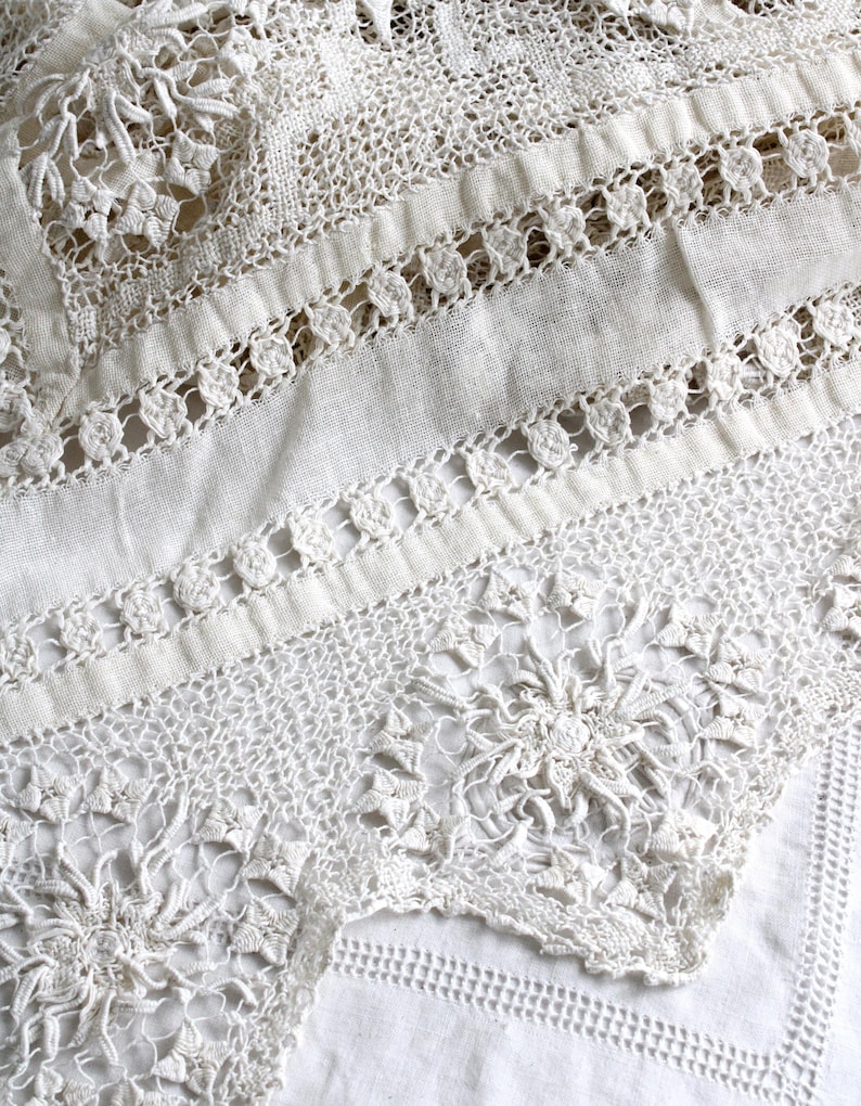 May include: Detailed close-up of a white lace textile. The lace displays a variety of patterns, including floral and geometric designs. The texture is intricate, with visible stitching and openwork, giving a delicate and elegant look. The textile appears to be a tablecloth or similar decorative item.