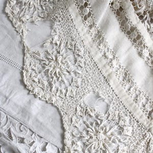 May include: Close-up of antique white lace textiles. The lace features intricate floral and geometric patterns, with a delicate, open weave. The textiles are layered, showcasing different textures and designs, ideal for vintage decor or crafting.