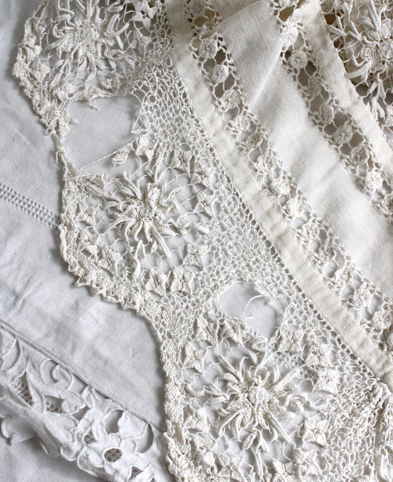 May include: Close-up of antique white lace textiles. The lace features intricate floral and geometric patterns, with a delicate, open weave. The textiles are layered, showcasing different textures and designs, ideal for vintage decor or crafting.