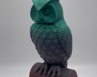 May include: A 3D printed owl figurine with a gradient of green to grey. The owl is perched on a brown log and is standing on a silver rotating base.
