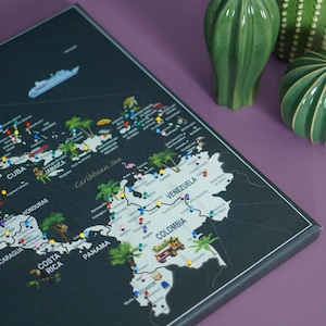 Può includere: Una mappa in bianco e nero dell'America centrale e dei Caraibi con puntine colorate che segnano le posizioni. La mappa è incorniciata e ha un bordo bianco. La mappa è su una superficie viola con decorazioni di cactus verdi.