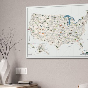 USA Travel Map, illustrated with top attractions for each state, hanged on a wall. The USA map is printed on canvas, the background is off white, while the land is light beige. In the right corner of the USA Map it is a personalization.