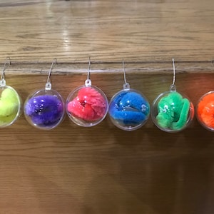 May include: Six clear glass baubles with colourful fuzzy worm-like toys inside. The baubles are hanging from silver hooks.