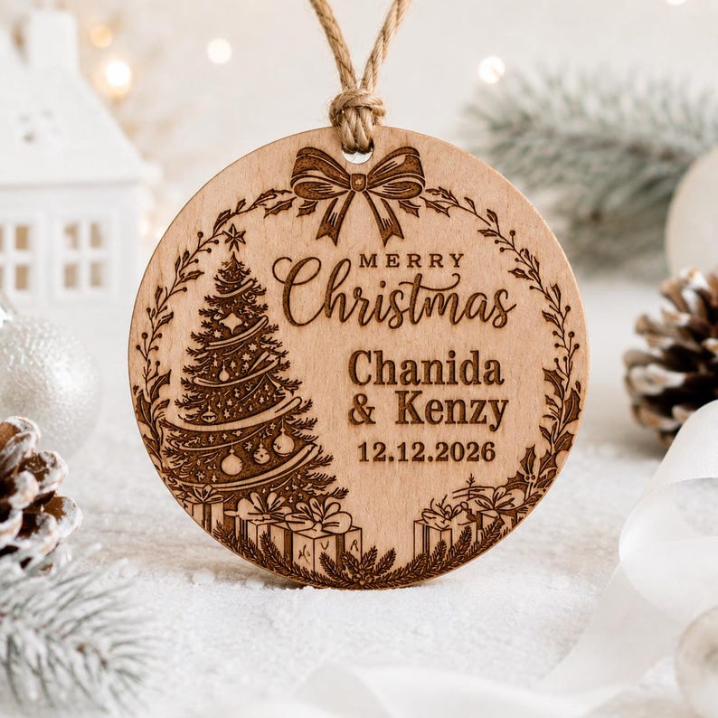 K&ouml;nnte beinhalten: Ein runder Weihnachtsanh&auml;nger aus Holz mit einer Lasergravur eines geschm&uuml;ckten Baumes, Geschenken und einer Schleife. Der Text lautet Merry Christmas, Chanida & Kenzy, und 12.12.2026. Der Anh&auml;nger h&auml;ngt an einer rustikalen Kordelschlaufe.