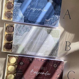 Könnte beinhalten: Drei Schachteln Pralinen mit dekorativen Deckeln. Jede Schachtel hat einen unterschiedlich gemusterten Deckel mit den Worten "HAYIRLI Bayramlar" in weißer Schrift. Die Pralinen sind in Reihen in den Schachteln angeordnet.