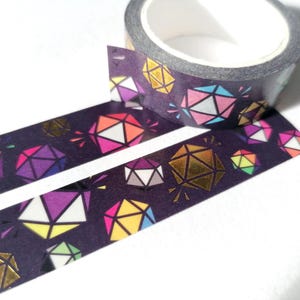 May include: A roll of washi tape with a dark purple background and a repeating pattern of colourful geometric shapes, including gold foil accents.