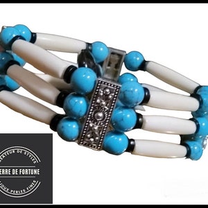 Peut inclure: Un bracelet en perles turquoise et blanches avec un fermoir argenté. Le bracelet porte une étiquette indiquant "Pierre de Fortune, Createur de Styles, Bijoux Perles Fines".
