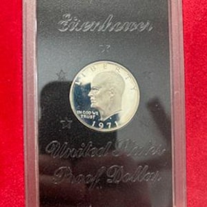May include: A 1971 United States Proof Dollar coin featuring the profile of a man, with the words "IN GOD WE TRUST" and "LIBERTY" visible. The coin is encased in a clear plastic holder with the words "Eisenhower" and "United States Proof Dollar" printed on a black background.