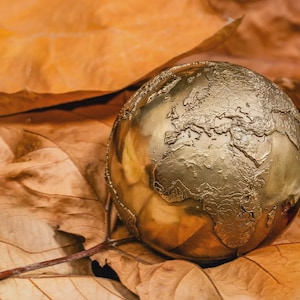 Puede incluir: Una esfera de metal dorado que presenta un mapa en relieve detallado de los continentes y océanos de la Tierra. El globo terráqueo tiene una superficie pulida y reflectante que capta la luz, resaltando los contornos geográficos de Europa, África y Asia.