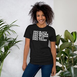 May include: A black t-shirt with the text "PRO BLACK PRO BROWN PRO WOMAN PRO GAY PRO TRANS" printed in white.