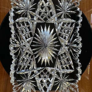 May include: A rectangular clear glass tray featuring an intricate cut pattern of radiating starbursts, geometric cross-hatching, and pointed arches. The edges of the tray are scalloped and serrated, creating a textured, reflective surface.