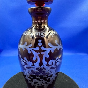 May include: A dark red glass decanter with a white etched floral design. The decanter has a matching stopper.