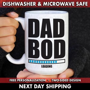 Peut inclure: Une tasse en céramique blanche avec un graphisme noir qui dit "DAD BOD" avec une barre de progression bleue qui dit "LOADING".