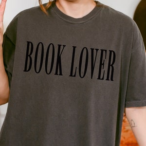 Op de afbeelding: Een donkergrijs T-shirt met de tekst "BOOK LOVER" in zwart gedrukt.