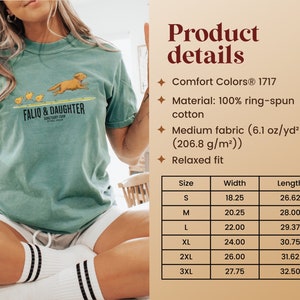 Op de afbeelding: Een tealblauw T-shirt met een afbeelding van een hond en kuikens die op een surfboard rennen. De tekst "FALIO & DAUGHTER" is op het shirt gedrukt. Het shirt is gemaakt van 100% ringgesponnen katoen en heeft een ontspannen pasvorm. De maattabel toont de breedte en lengte van het shirt in inches.