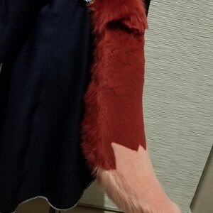 May include: A plush, red fox tail with a light pink tip. The tail is attached to a dark blue garment with a decorative floral patterned belt. The tail is made of soft, faux fur.